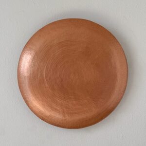 Lámpara en forma de disco de cobre martillado con textura circular, similar a un eclipse.