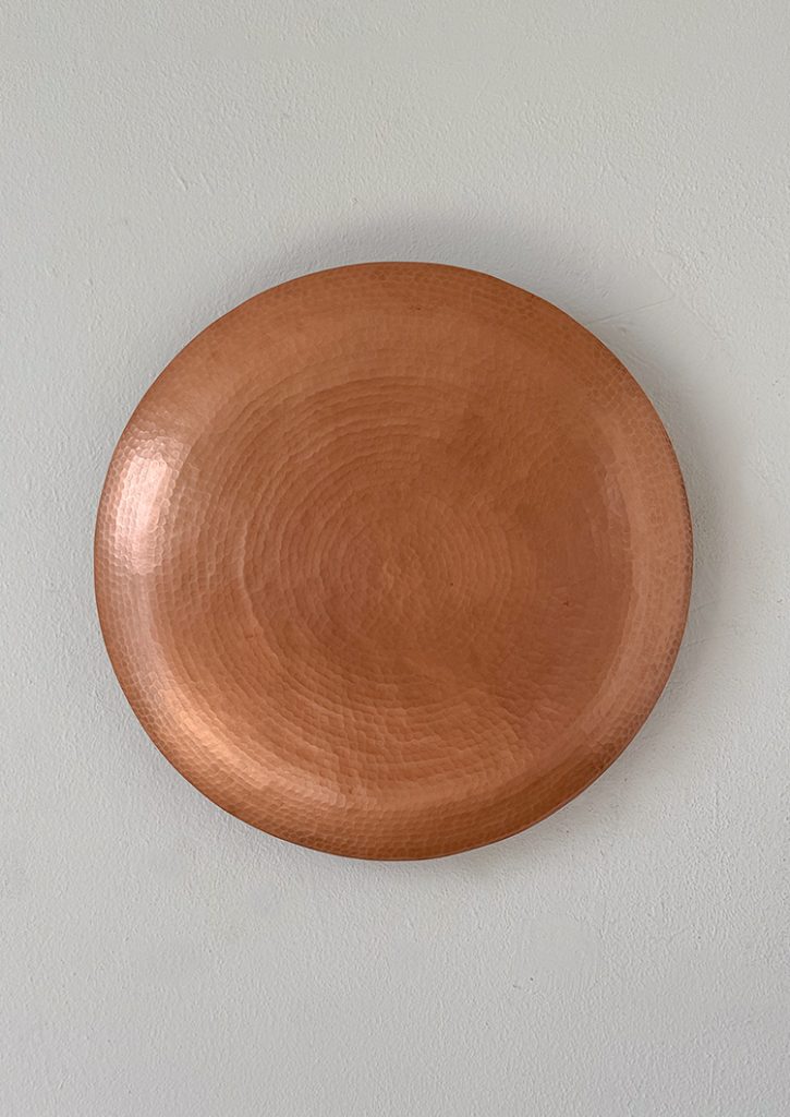 Lámpara en forma de disco de cobre martillado con textura circular, similar a un eclipse.
