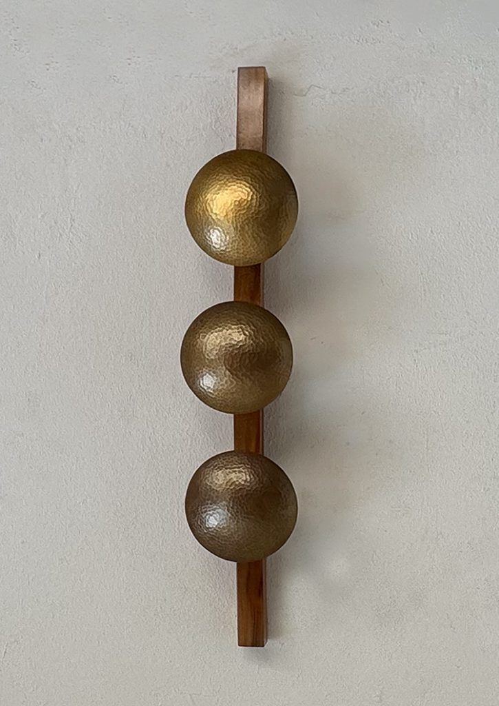 Lámpara Orion: tres esferas doradas martilladas en una tabla de madera.